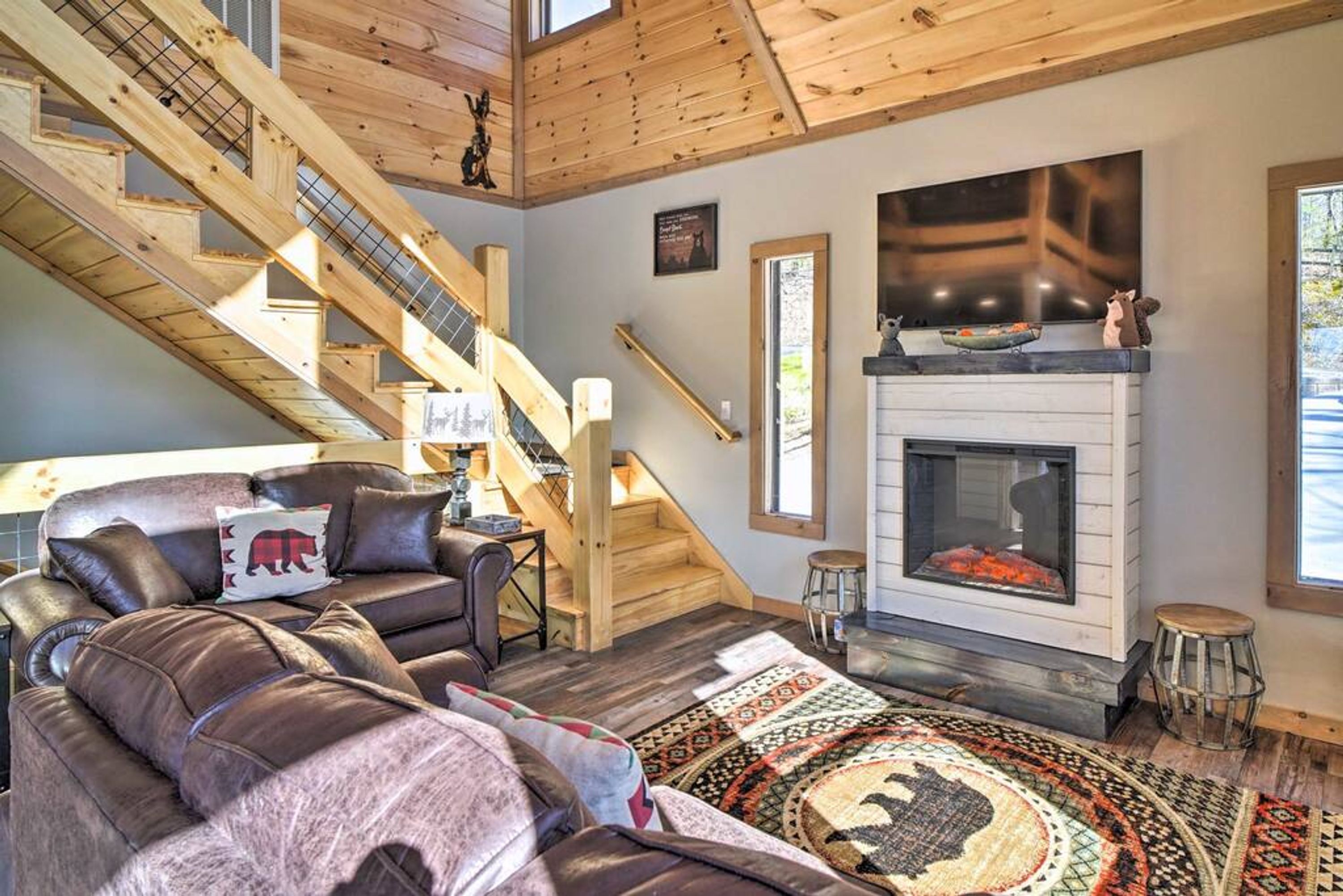 A spacious living room with a fireplace, a wooden staircase, and a large window.