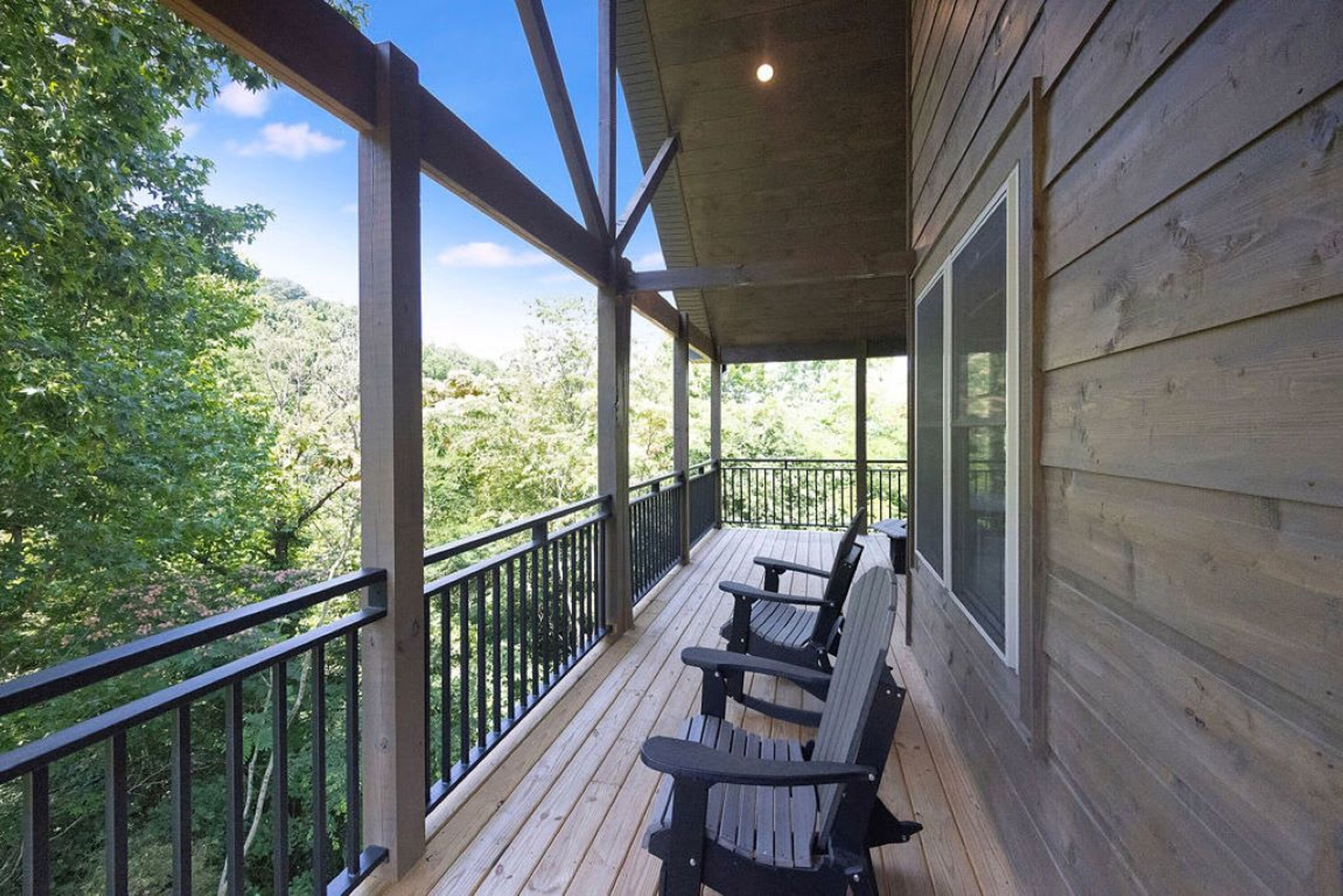 A wooden deck with a railing, two Adirondack chairs, and a view of a forested area.