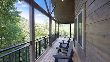 A wooden deck with a railing, two Adirondack chairs, and a view of a forested area.