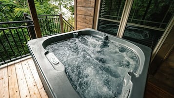 A hot tub on a wooden deck with a wooden wall and windows in the background.