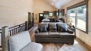 A spacious living area with a wooden ceiling, a sofa, a coffee table, and a kitchen in the background.