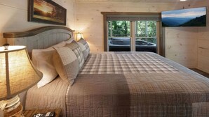 A bedroom with a large bed, wooden headboard, a television, and a window with a view of trees.