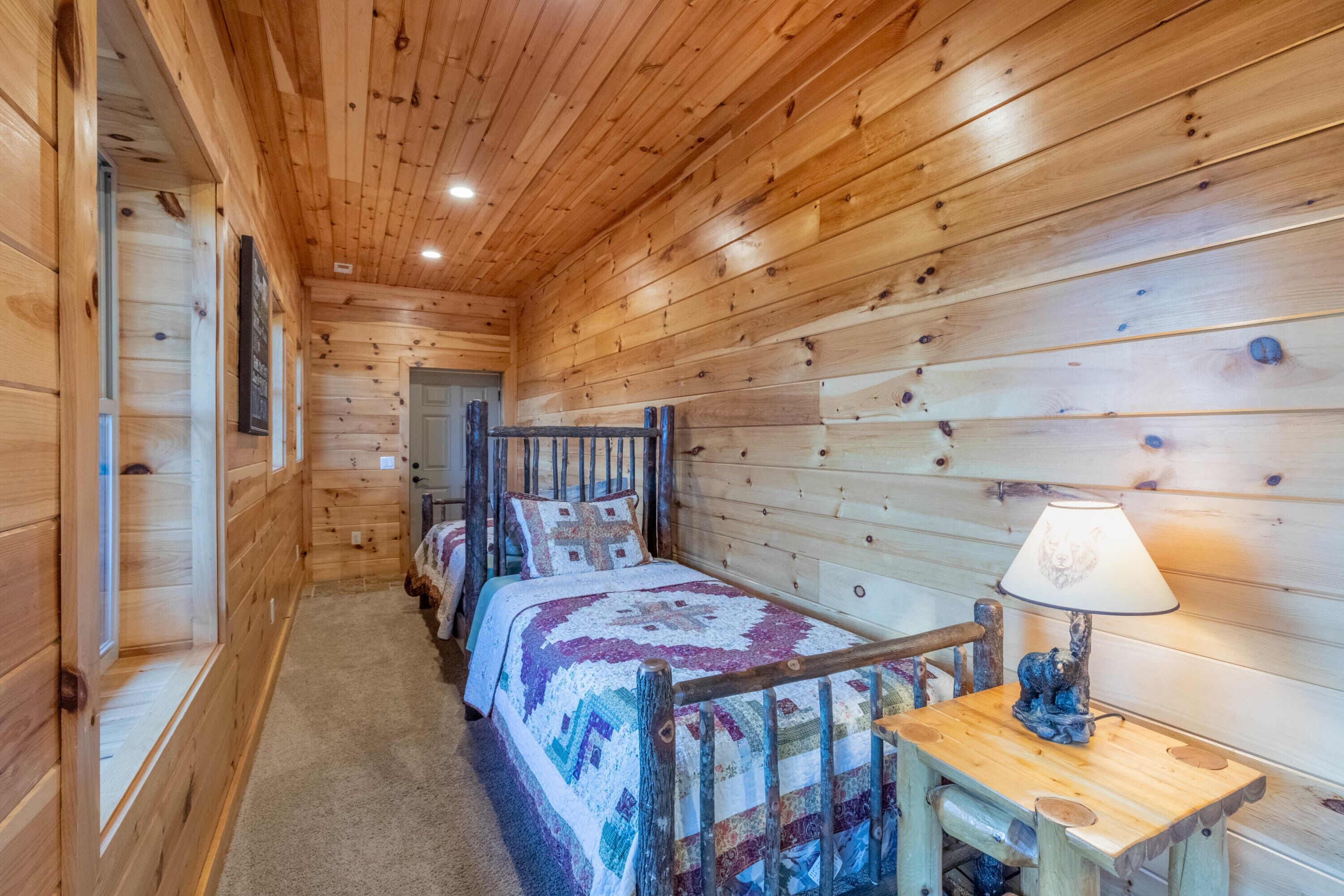 A wooden cabin room with a bed, a chair, and a table with a lamp.