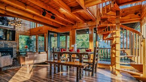 A spacious wooden interior with a fireplace, dining area, and a wooden staircase. - Mountain Majesty With Spectacular Views (Sevierville)