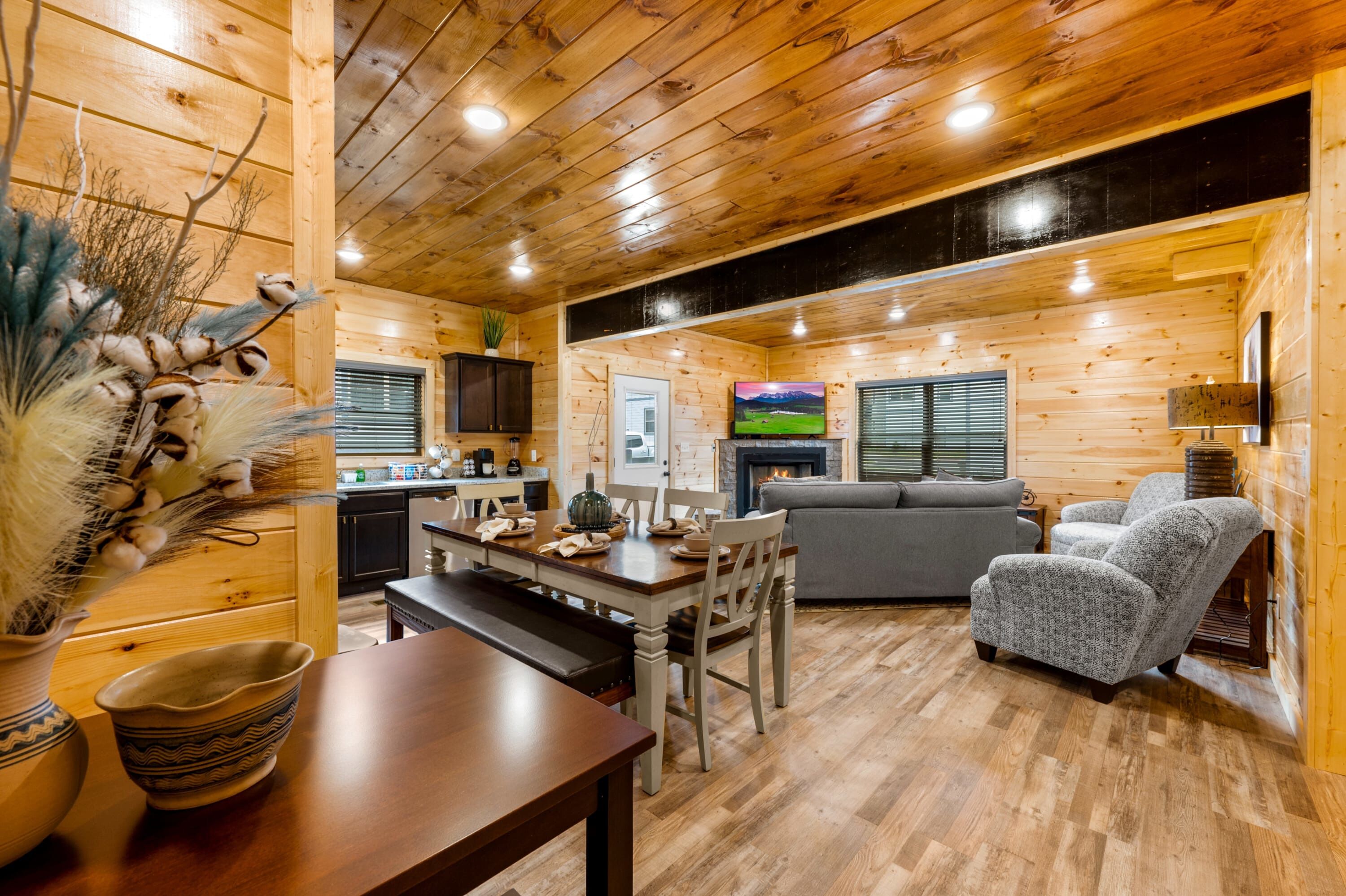 A cozy cabin interior with a wooden dining table, a sofa, and a fireplace.