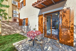 A patio with a table and chairs, a door to a room, and a small garden area. - Holiday apartment with air conditioning (Rovinj)