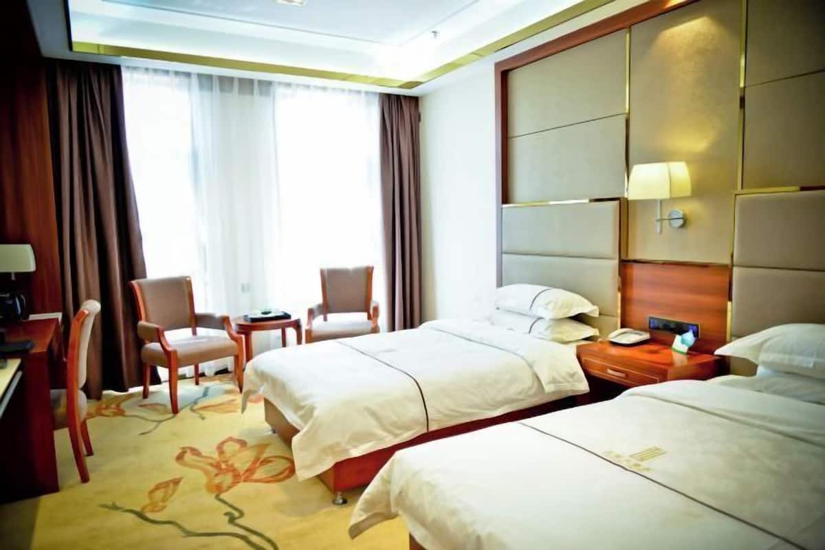 Habitación de hotel con dos camas, un escritorio, sillas y un ventanal con cortinas.