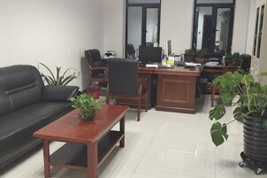 Una sala de estar amoblada con un sofá, una mesa de centro de madera, un escritorio con computadora y plantas en macetas.