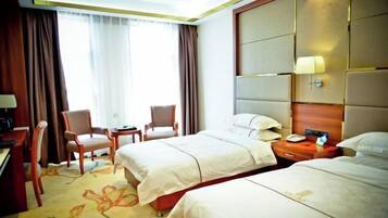 Quarto de hotel com duas camas, uma escrivaninha, uma cadeira e uma mesinha.