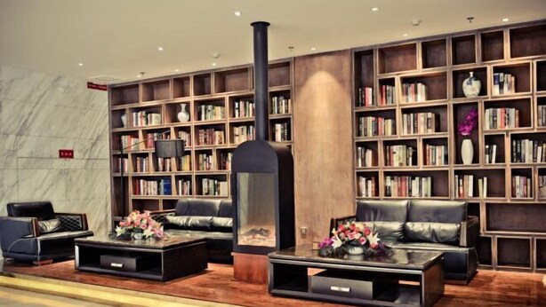 A modern library with leather sofas, a large bookshelf, and a central fireplace. - Tianyue Hotel (Fuyun)