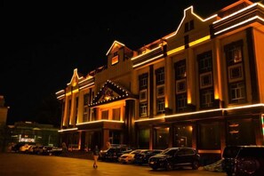 A building with multiple floors, large windows, and a parking lot with cars. - Tianyue Hotel (Fuyun)