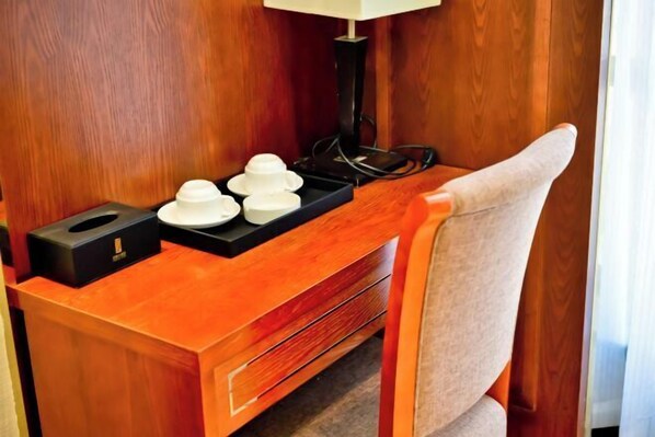 A wooden desk with a lamp, a tissue box, and a tray with cups.