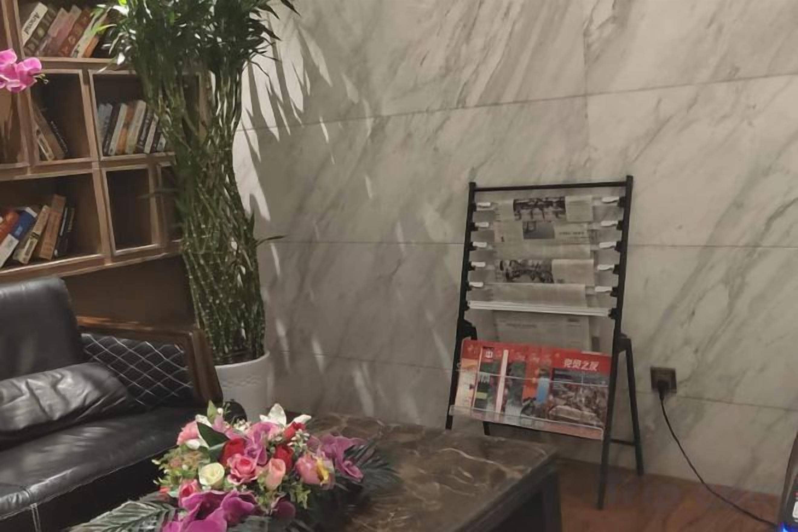 A marble wall, a bookshelf, a potted plant, a coffee table with flowers, and a magazine rack.