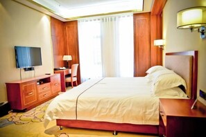 Una habitación de hotel con cama, escritorio, silla, televisor y ventana con cortinas.