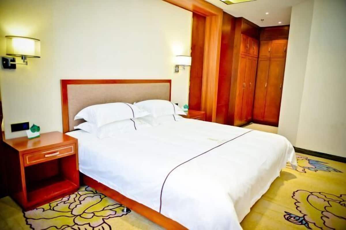 Una habitación de hotel con una cama grande, un armario de madera y una mesita de noche con lámpara.