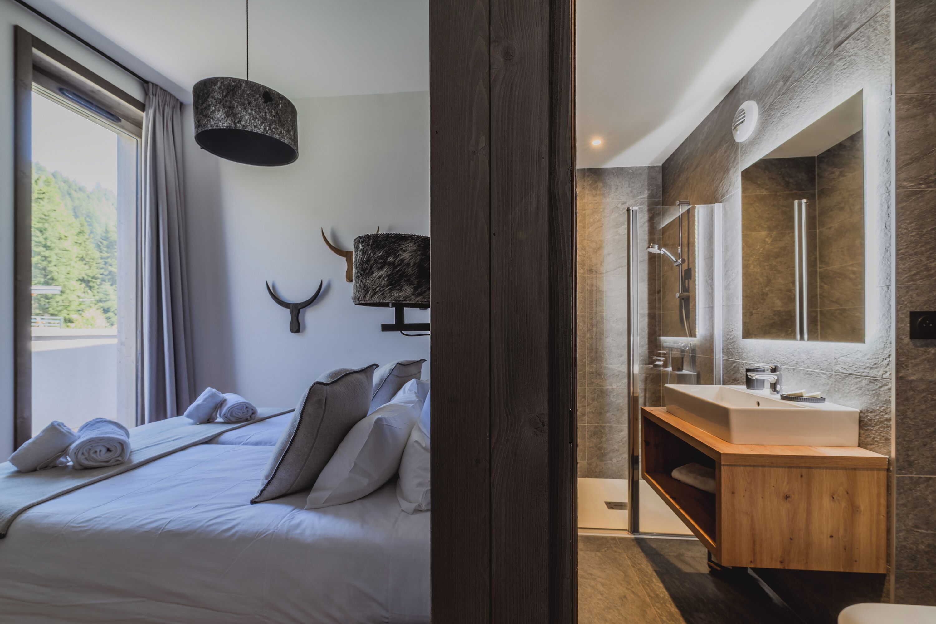 Une chambre moderne avec un grand lit, une coiffeuse en bois et une salle de bain dotée d’un grand miroir et d’une douche.