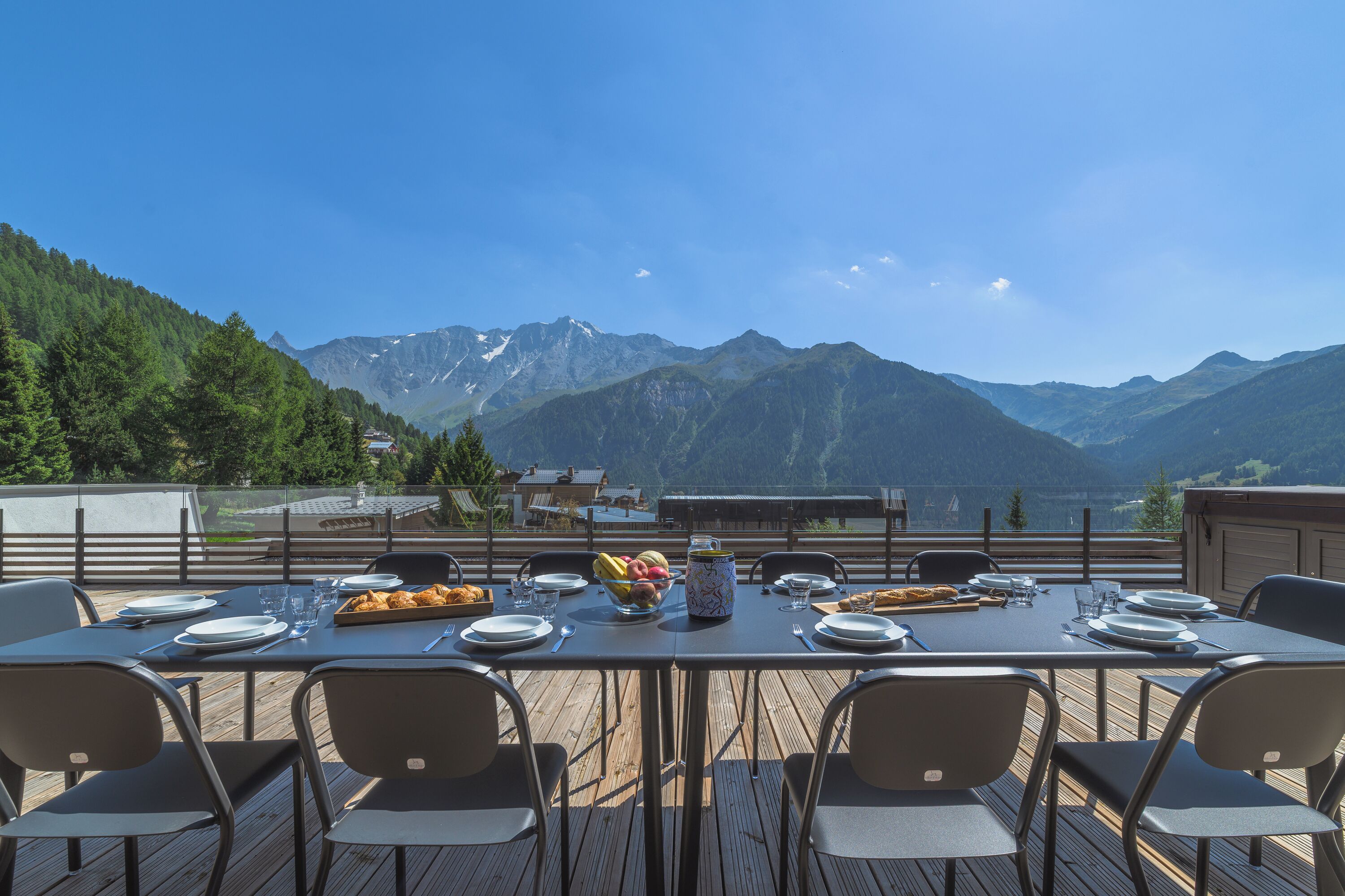 A dining table set outdoors with a mountain view, surrounded by chairs.