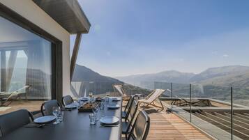 Une table à manger pour quatre personnes, avec vue sur les montagnes, des sièges d’extérieur et une balustrade en verre.
