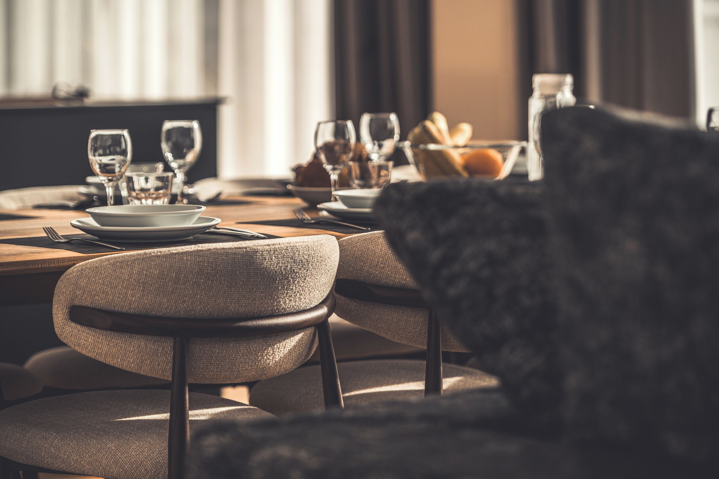 A dining table set with plates, glasses, and a bowl of bread.