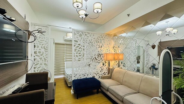 A modern living room with a sofa, a TV, and decorative wall panels. - Taguig 1 Bedroom with Balcony Near Bgc (Taguig)