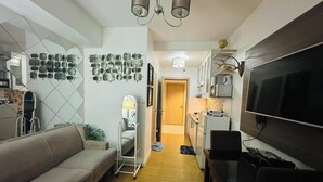 A living room with a sofa, a TV, and a kitchen area with cabinets and a microwave. - Taguig 1 Bedroom with Balcony Near Bgc (Taguig)