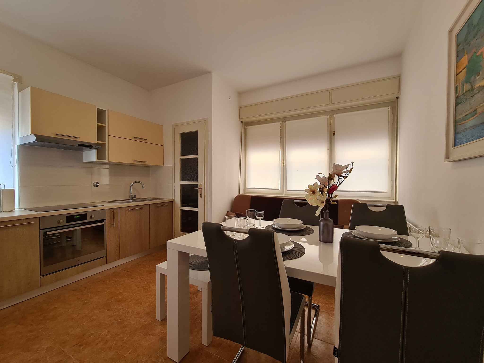 Uma cozinha moderna com armários brancos, forno embutido e área de jantar com mesa branca e cadeiras pretas.