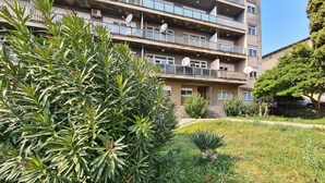 A multi-story residential building with balconies, satellite dishes, and a well-maintained garden area with various plants and flowers.