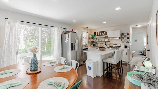 A modern kitchen with white cabinets, a central island, and a dining area with a wooden table and chairs.