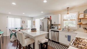 A modern kitchen with white cabinets, stainless steel appliances, a central island, and a dining area with chairs and a table.
