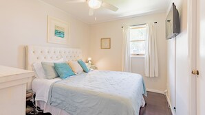 A bedroom with a large bed, a ceiling fan, a nightstand, and a TV mounted on the wall.
