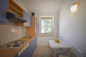 Cocina compacta con estufa a gas, armarios de madera, una ventana y una pequeña mesa de comedor con fruta.