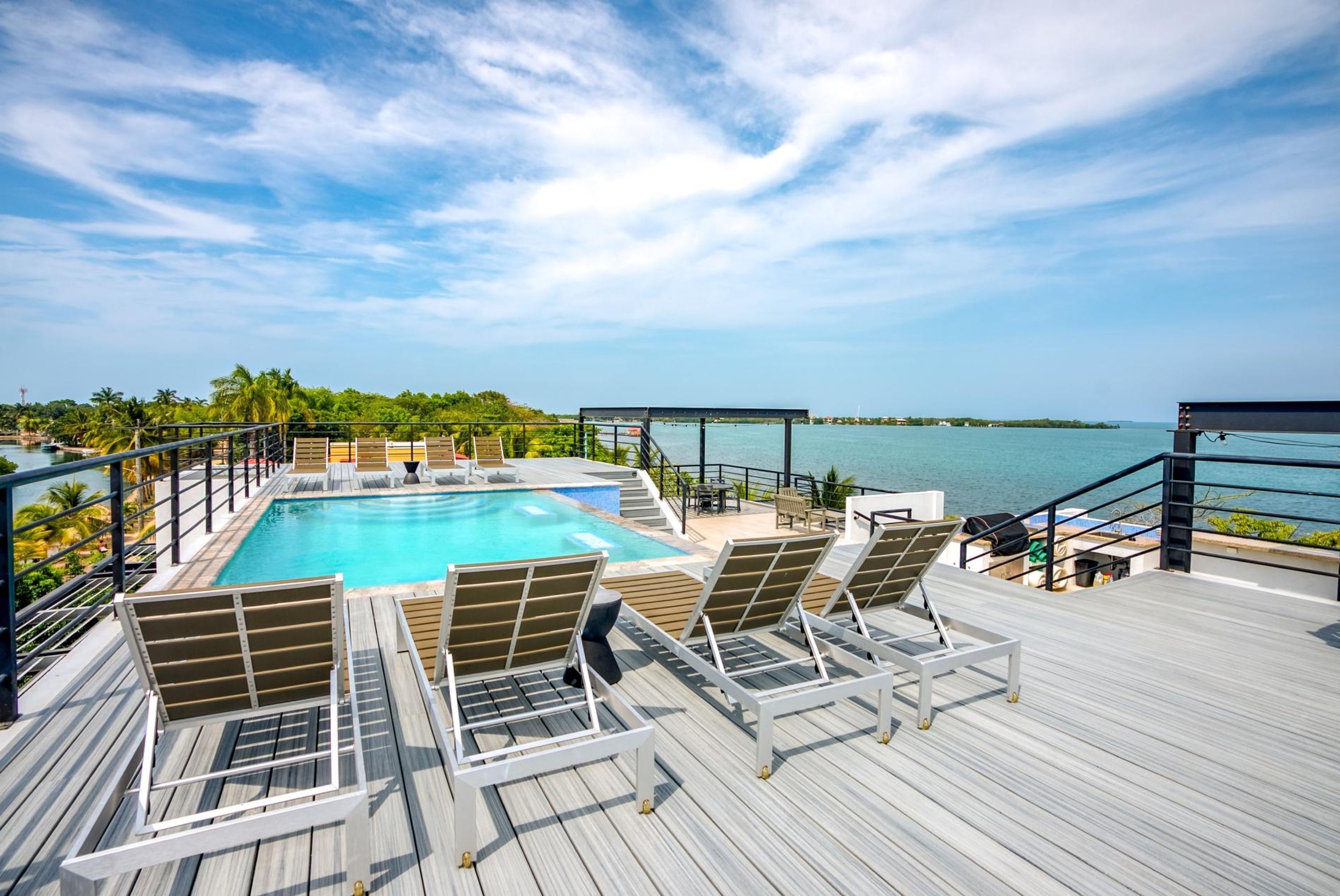 A poolside area with lounge chairs, a pool, and a view of the ocean.