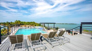 A poolside area with lounge chairs, a pool, and a view of the ocean.