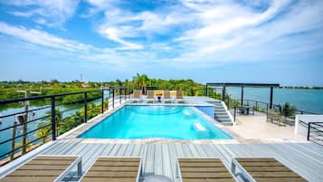 A pool with a wooden deck, lounge chairs, and a view of the water.