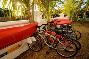 Una bicicleta estacionada junto a un barco rojo, con un muro blanco y palmeras al fondo.