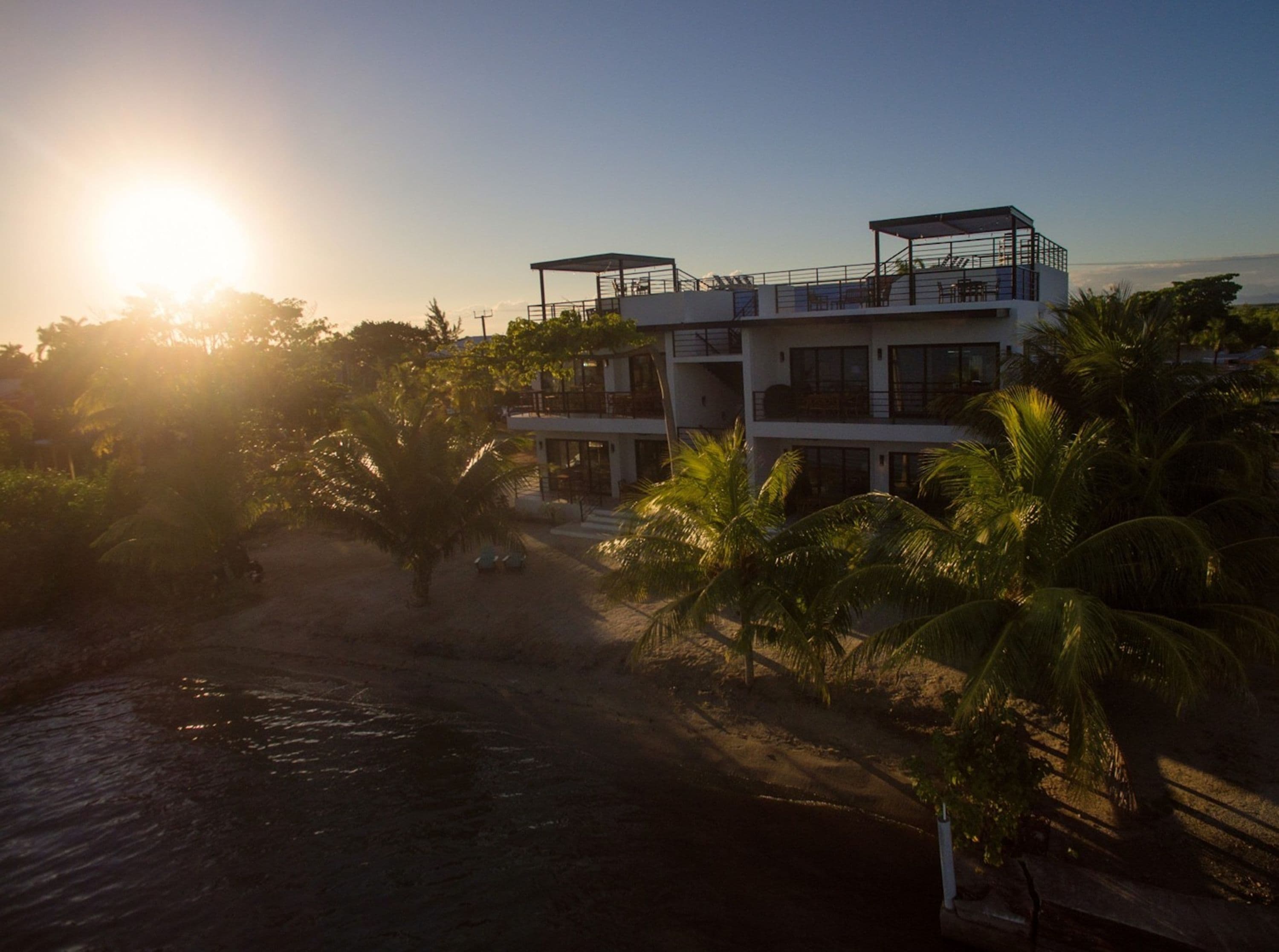 A multi-story building with a balcony, surrounded by palm trees and a body of water.