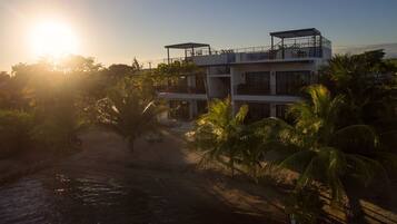 A multi-story building with a balcony, surrounded by palm trees and a body of water.