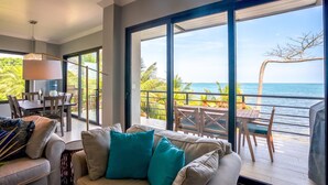 A spacious living area with a large window overlooking a balcony with a view of the ocean. - Oceanfront Sunset Gecko Condo - Second Floor 2A (Placencia)
