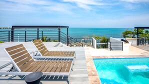A poolside area with lounge chairs and a view of the ocean. - Oceanfront Sunset Gecko Condo - Second Floor 2A (Placencia)