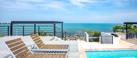 A poolside area with lounge chairs and a view of the ocean.