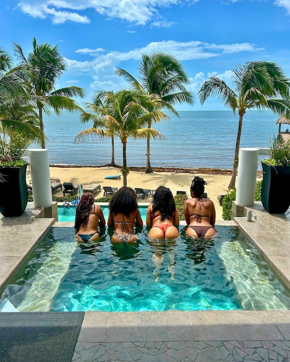 Una piscina con agua cristalina, rodeada de palmeras y vista a la playa.
