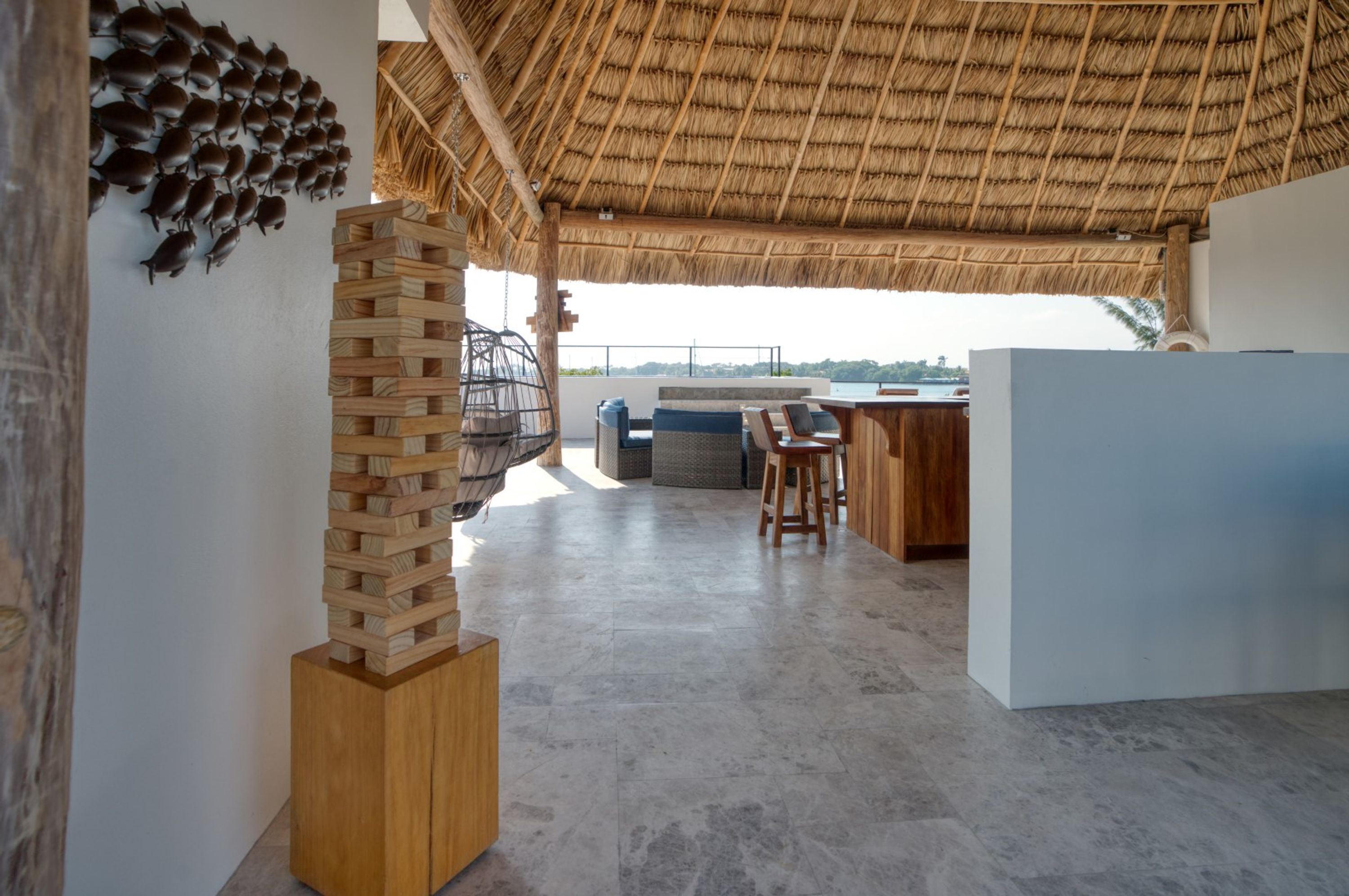 A spacious room with a high ceiling, a thatched roof, a wooden play structure, and a view of the sea.