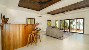 A spacious living area with a wooden bar, a grey sofa, and a large sliding glass door leading to an outdoor patio.