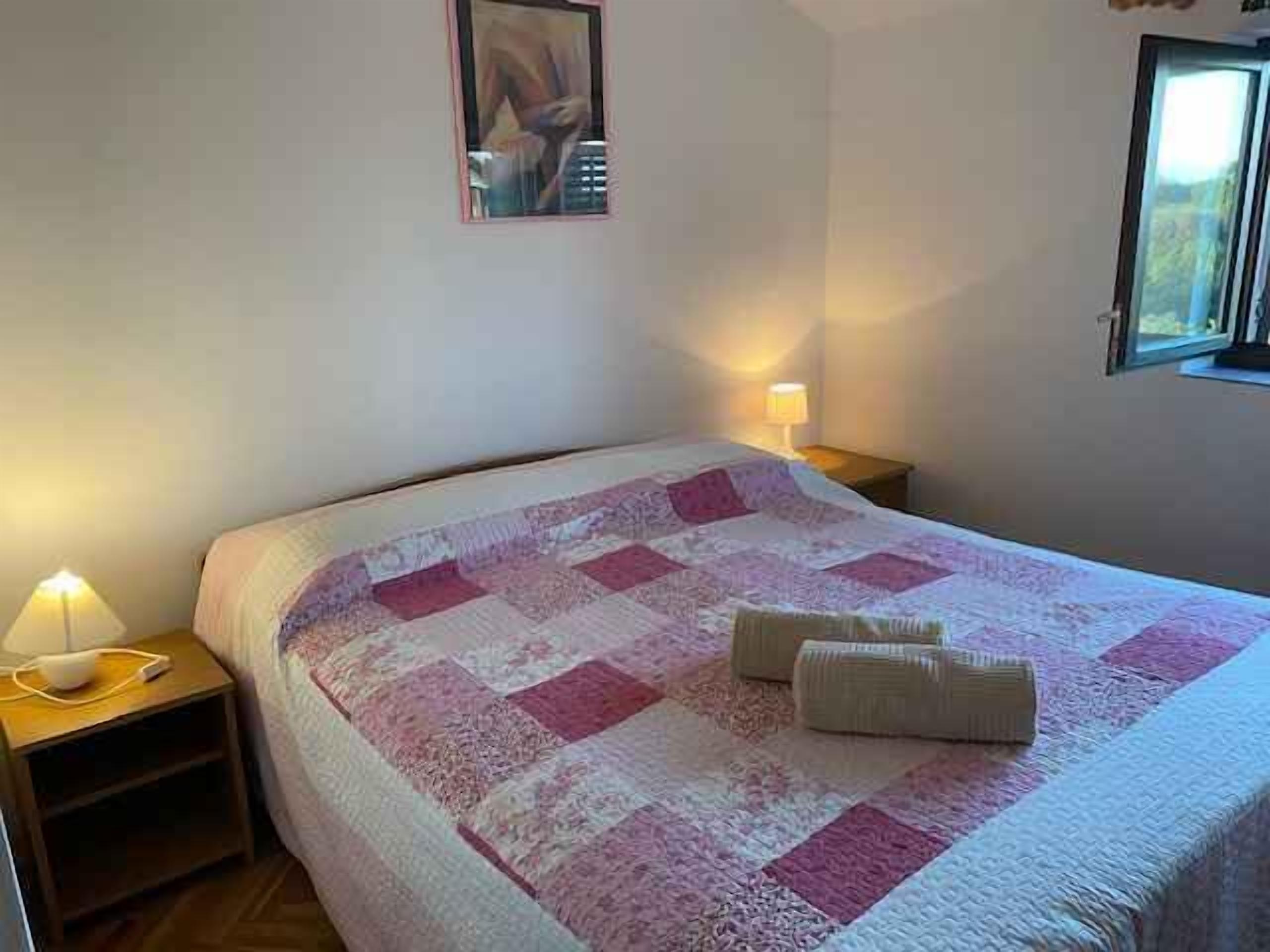 A neatly made bed with a patterned bedspread, two bedside lamps, and a framed picture on the wall.
