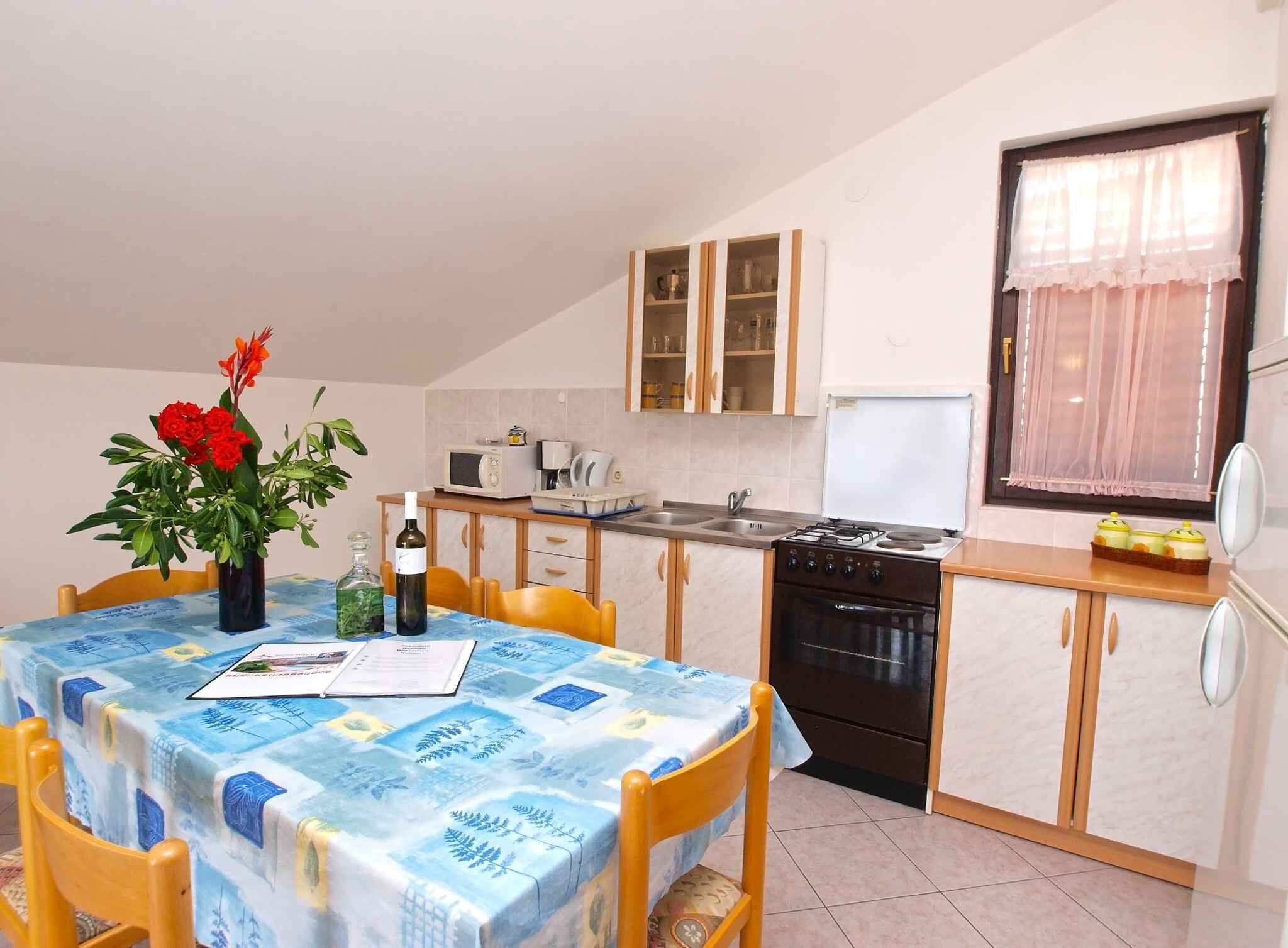 Una cocina compacta con comedor, que incluye una mesa con mantel azul, sillas de madera, un jarrón con flores rojas y una botella de vino.