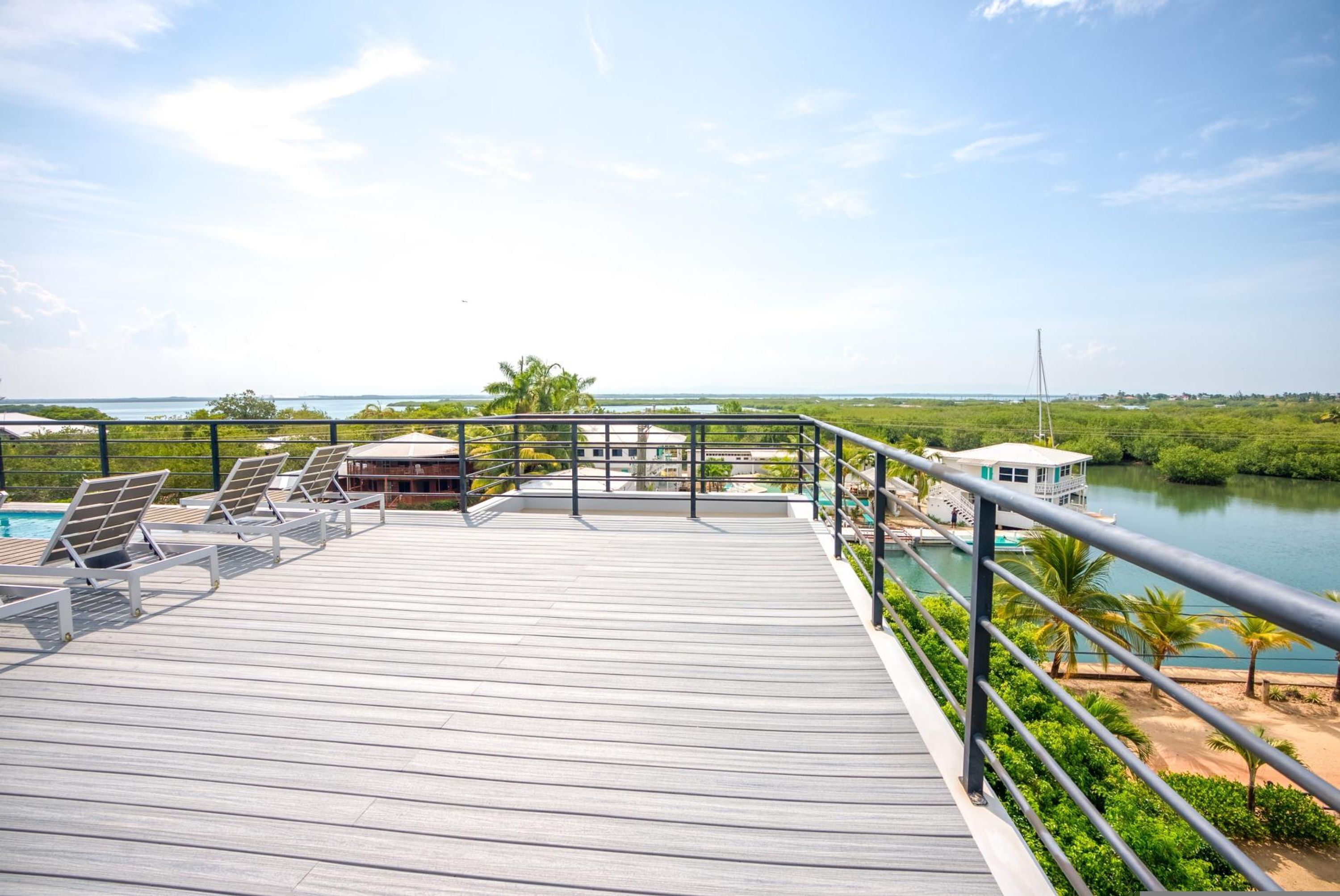 Una terraza de madera con sillones de descanso que da a una masa de agua, un barco amarrado cerca y vistas del paisaje circundante.