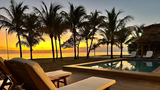 A poolside area with lounge chairs and a view of the sunset over the ocean.