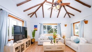 A spacious living room with a wooden ceiling, a television, a sofa, a coffee table, and a cabinet.