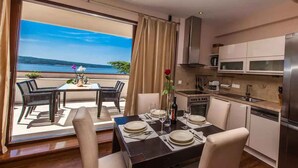 A dining area with a table set for four, a kitchen with modern appliances, and a view of the sea through large windows. - Holiday apartment with air conditioning and sea view (Crikvenica)