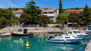 A marina with boats docked, a stone wall, and buildings with red roofs in the background. - Holiday apartment with air conditioning and sea view (Crikvenica)